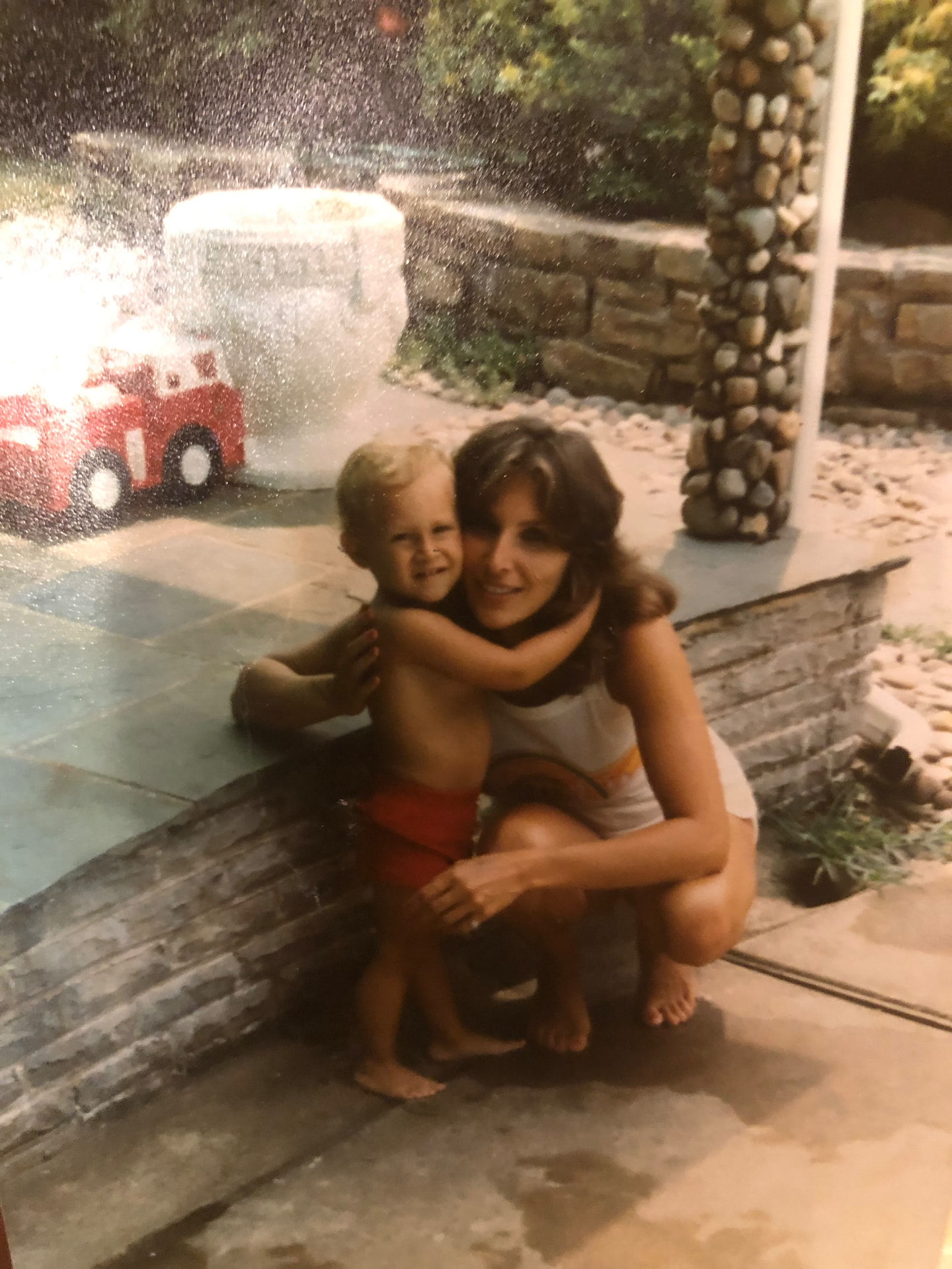 A young Harrise crouching beside a pool, embracing her young child