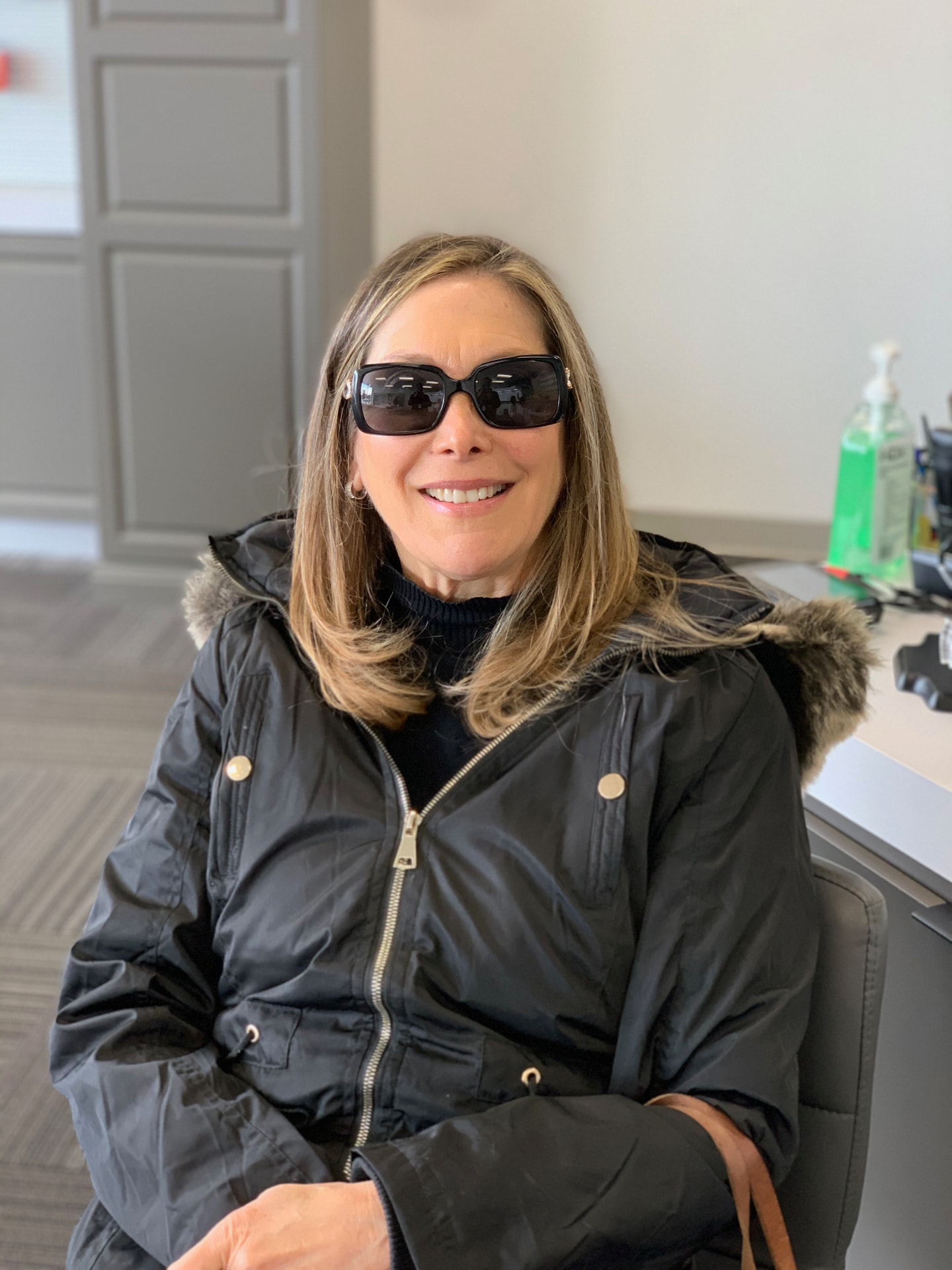 Harrise smiling, wearing sunglasses and a black coat
